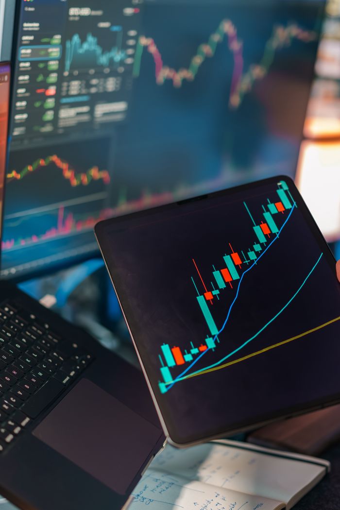 The Art of Drawing Readers In: Your attractive post title goes here A tablet displaying a candlestick chart with a laptop screen showing stock market data for financial analysis.